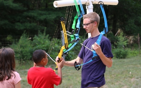 Archery instructor hands boy a bow