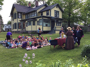 A group of children sit on the Mann House lawn during a program