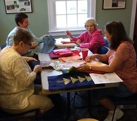 Four women hand-sew quilt pieces at a table