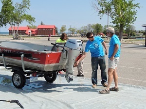 Volunteers at an Aquatic Invasive Species Lansing Blitz event at a boat launch show a boater how to check for and remove aquatic plants.