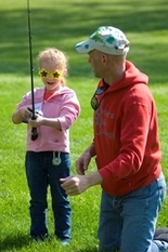 young girl holding fishing pole, dad kneeling next to her