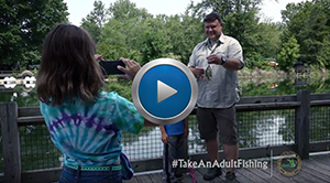 still frame from Take an Adult Fishing video - girl taking photo of man holding fish