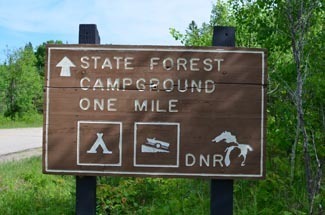 A sign shows a Michigan state forest campground ahead, a rustic adventure awaits.