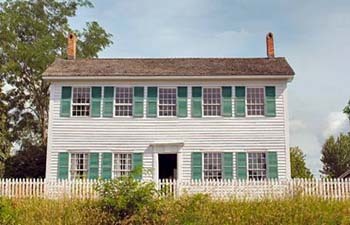 Walker Tavern, a two story white wood-framed building with green shutters, stands on a rise above US12 in Brooklyn, MI