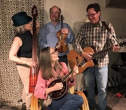 Two men and two women with guitars and mandolins are standing together and laughing. 