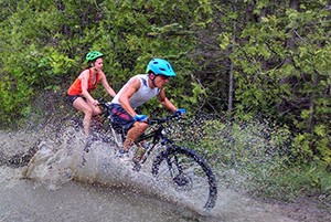 two participants riding bikes through water