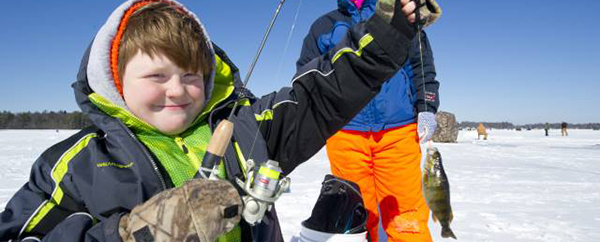boy on frozen lake holding up fish he caught