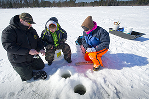 instructor showing two students ice fishing techniques on frozen lake