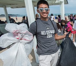 A young man holds a bag of trash collected at a beach cleanup - via Alliance for the Great Lakes 