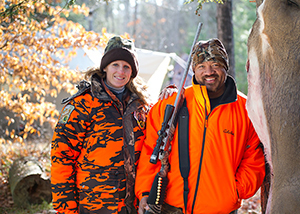 male and female deer hunters in camo and hunter orange with hunting rifle