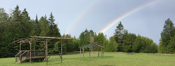 Two bark structures in a green field with a double rainbow in the skyline