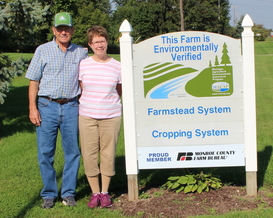 Two farmers stand in front of a MAEAP verification sign