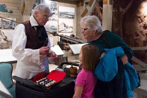A docent dressed as a 19th century doctor shows period medical instruments to two visitors.