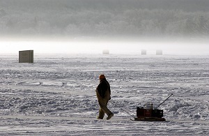 A bundled-up fisherman pulls a loaded sled along a frozen Michigan lake