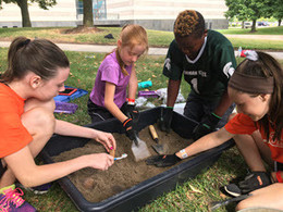 Four children dig in a large bin of dirt during Dig Camp