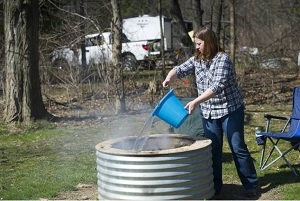 a woman pouring water on a campfire in a ringed fire pit