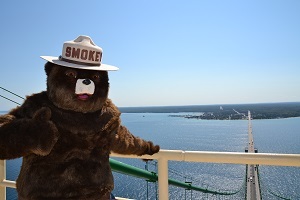 Smokey Bear waving from atop the Mackinac Bridge in the Straits of Mackinac, blue sky in the background