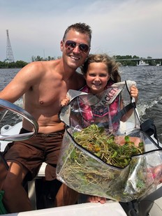 A man and little girl on a boat holding collected European frogbit, an invasive aquatic plant in Michigan