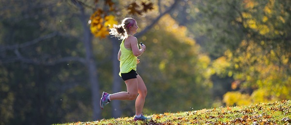 Profile view of a woman wearing shorts and a tank top, running on a trail, autumn background