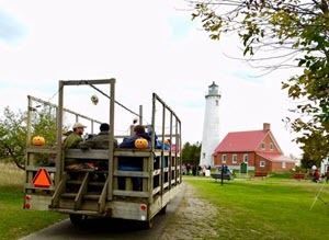 A tractor pulls a wagon filled with people and hay. Lighthouse is in the background