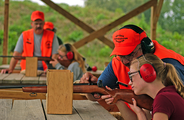 A hunter safety instructor helps a young girl learn about safe firearm handling