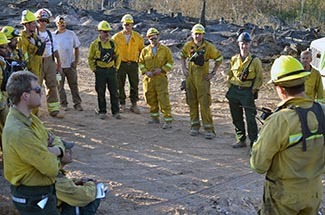 Firefighters stand in a circle for an evening briefing on an active fire.