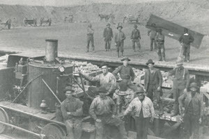 black and white historic photo of men standing in front of the locomotive