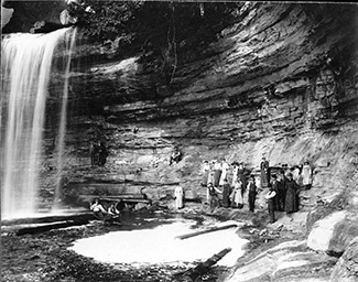 An early-1900s photo shows people underneath the Upper Tahquamenon Falls.