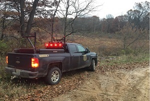 black Michigan DNR conservation officer truck, brake lights on, in a forested swamp area