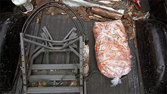 A bag of deer bait and a tree stand are shown in the bed of a pick-up truck.