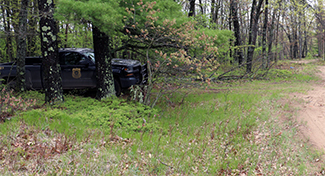 A conservation officer patrol vehicle is parked near a woods road.
