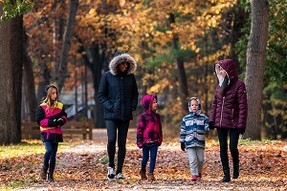 Adults and small children dressed in fall jackets, walking down a tree-lined trail at Sleeper State Park