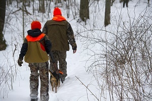 back view of adult and youth hunters, wearing hunter orange, walking down a snowy trail