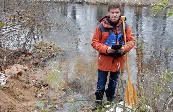 A Trout Unlimited volunteer, Parker Vandenberg, stands by a river and adds in monitoring data.
