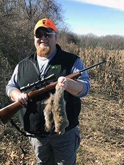 The author is pictured outdoors with a squirrel after a successful hunt.