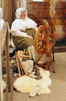 A women dressed in historic clothing sits at a spinning wheel