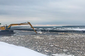 A backhoe is used to clear stamp sands from the Grand Traverse Harbor.