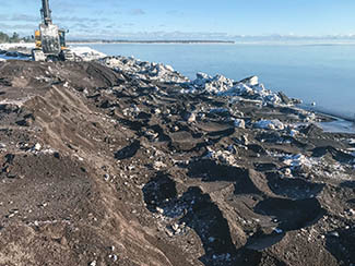 A backhoe removes stamp sands from an area north of the breakwater at the Grand Traverse Harbor.