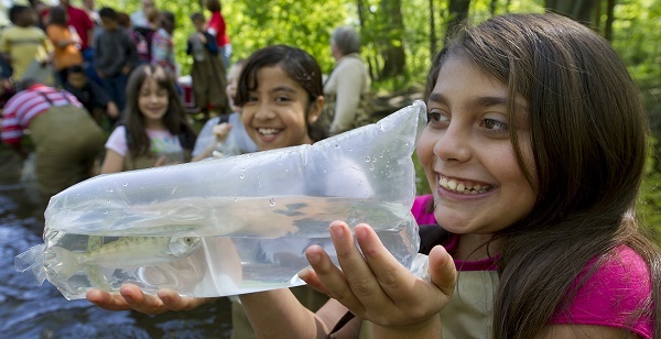 dark-haired, smiling girl holding a live, bagged salmon, ready for release into the water