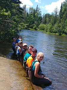group of students in waders sitting with legs in river
