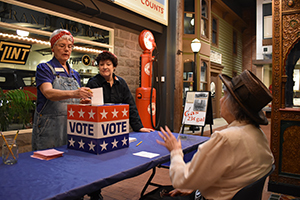 Two women dressed as Rosie the Riveter discuss voting with a woman dressed as a 1920s suffragette.