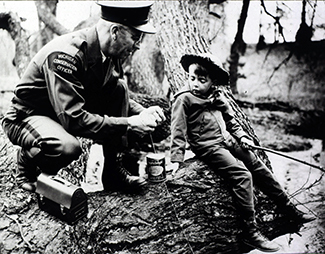 In a historic photo, a conservation officer shows a young boy how to tie a fishing knot.