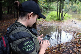 A female conservation officer is shown on a fishing patrol, using technology to check property lines.