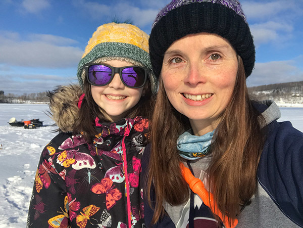 A DNR fisheries biologist and her daughter smiling as they enjoy an ice fishing outing.