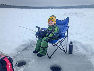 A young boy in a chair sits with an ice fishing pole jigging for bluegill.