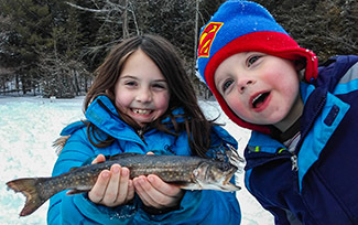 Two young children dressed for winter show off a splake they caught while ice fishing.