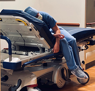 An exhausted healthcare worker rests on a medical bed.