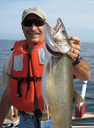 smiling man standing up in boat, holding a lake trout