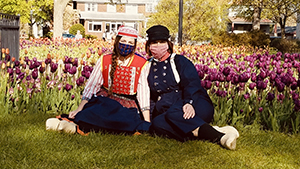 COVID Collecting: Two woman with masks and wooden shoes sit in front of a tulip garden.
