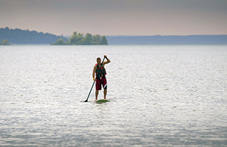 A man uses a paddle board on calm waters.